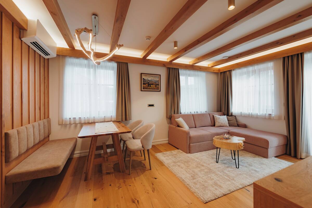 A modern living room with wooden beams, a sofa, a dining table with chairs, and a bench.