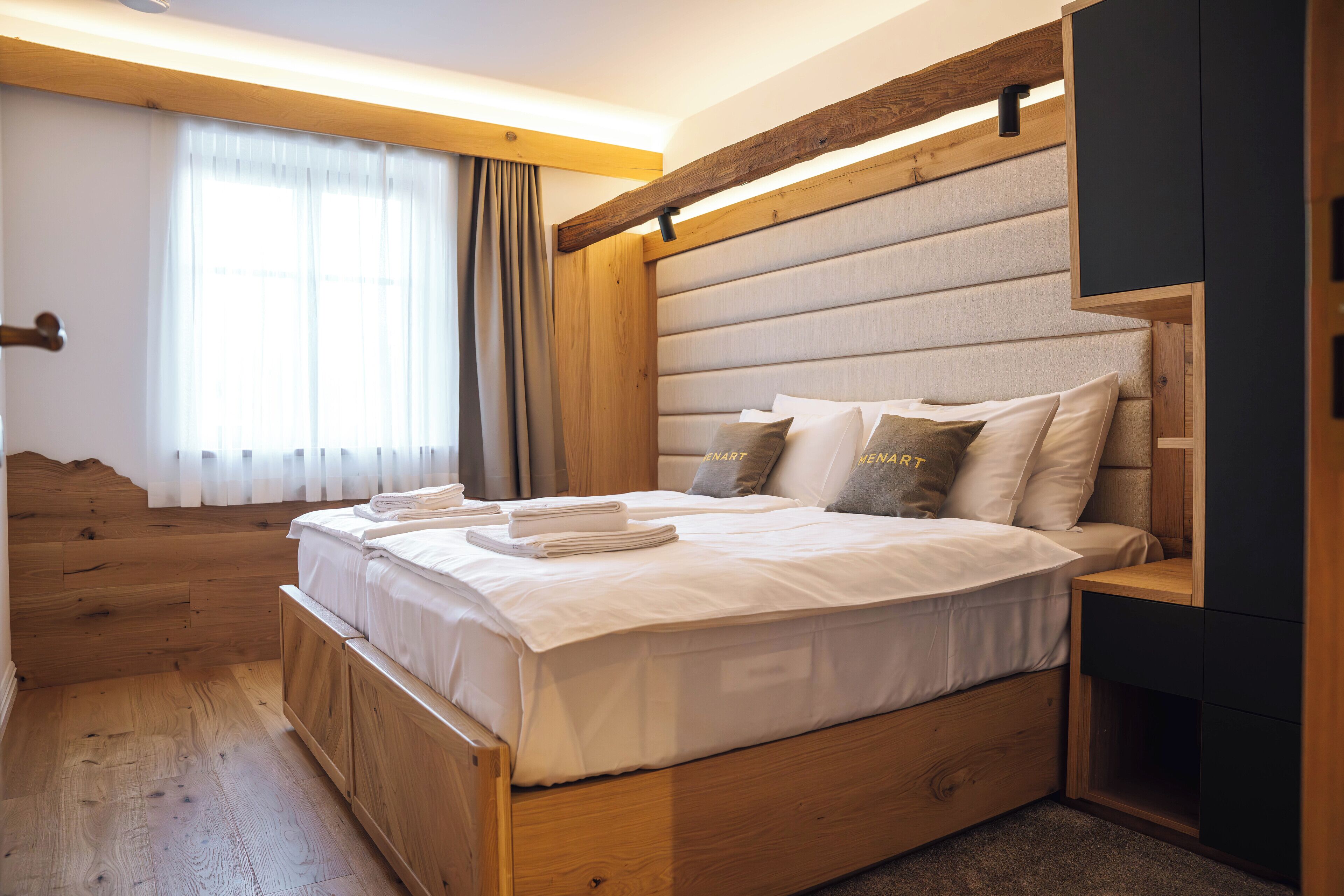 Un dormitorio moderno con cabecera de madera, una cama grande con sábanas blancas impecables y una mesita de noche empotrada.