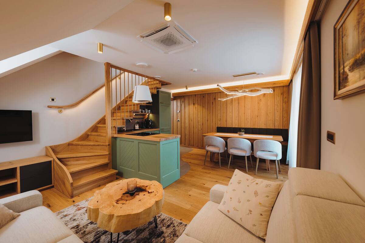 A modern interior with a wooden staircase, a kitchen island, a dining area, and a living room with a sofa and coffee table.