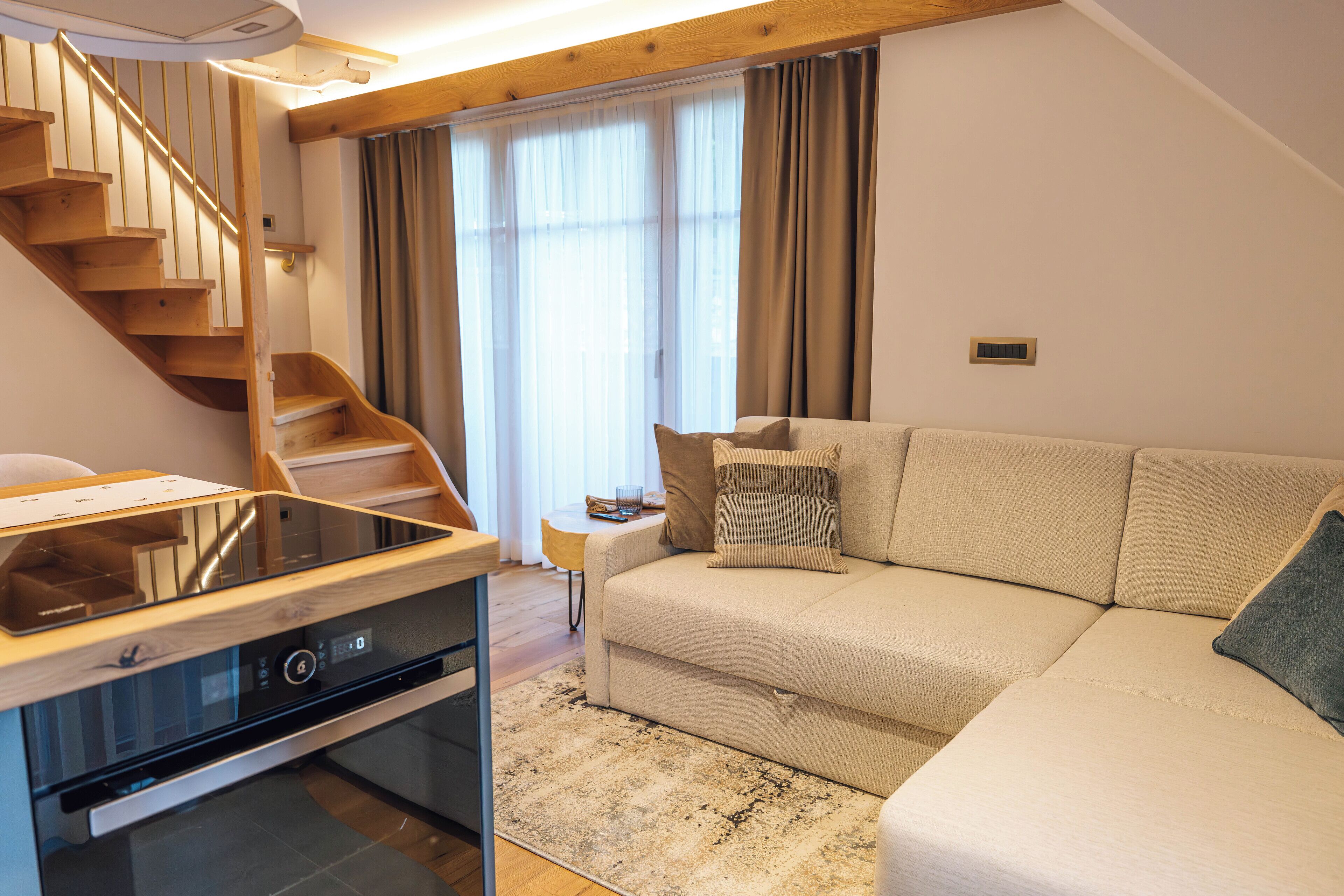 A modern living room with a wooden staircase, a sofa, a small table, and a built-in oven.