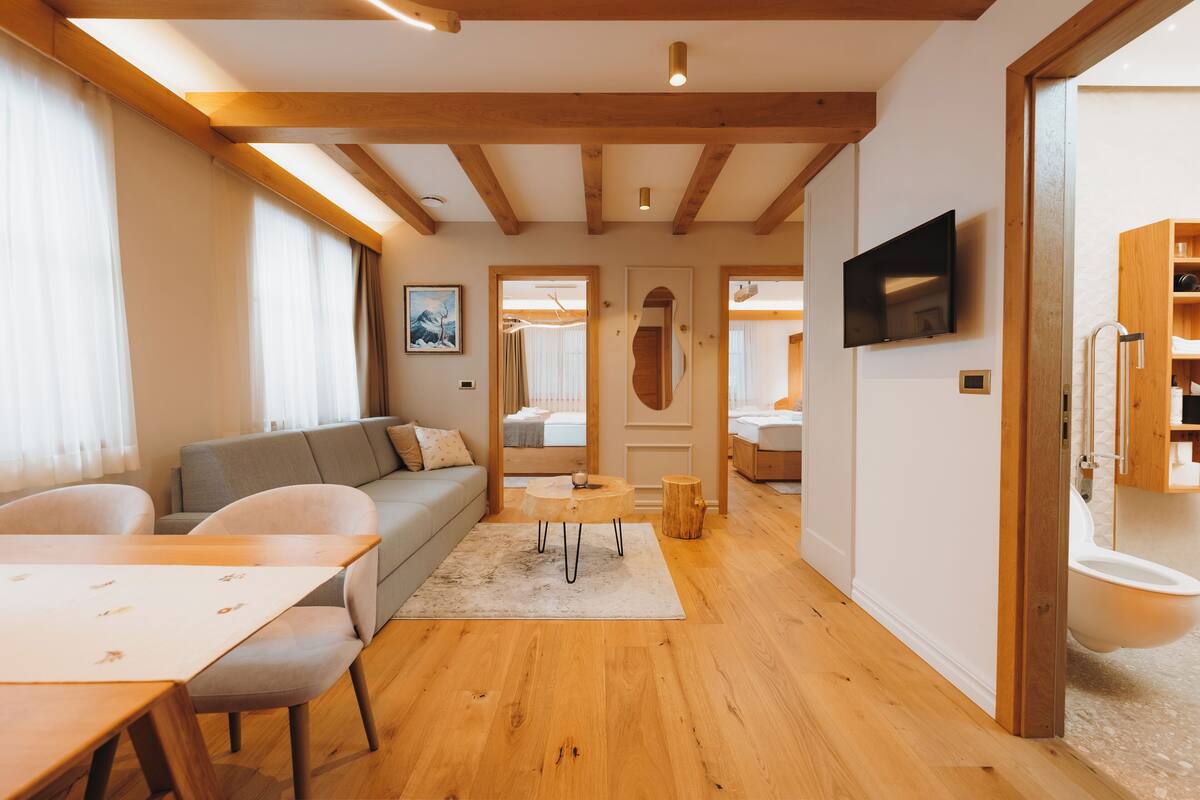 A modern living room with a wooden floor, a sofa, a dining table, and a TV mounted on the wall.