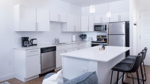 A modern kitchen with white cabinetry, stainless steel appliances, and a central island with bar stools. - Sugarhouse-1BR 1BA Great Views! (Salt Lake City)