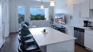 A modern kitchen with a central island, white cabinetry, and a dining area with a view of the outdoors. - Sugarhouse-1BR 1BA Great Views! (Salt Lake City)