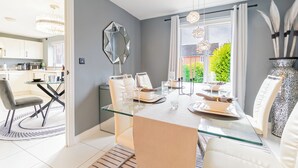 A modern dining area with a glass table, white chairs, and a view of the garden through large windows. -  Birmingham Stay Free Parking for Families Travellers Professionals M6 (Birmingham)