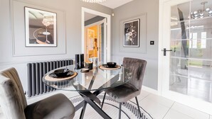 A modern dining area with a glass table, grey upholstered chairs, and framed artwork on the walls. -  Birmingham Stay Free Parking for Families Travellers Professionals M6 (Birmingham)