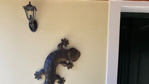 Una escultura de metal en forma de salamandra montada en la pared, un accesorio de luz también en la pared, y una silla de madera.