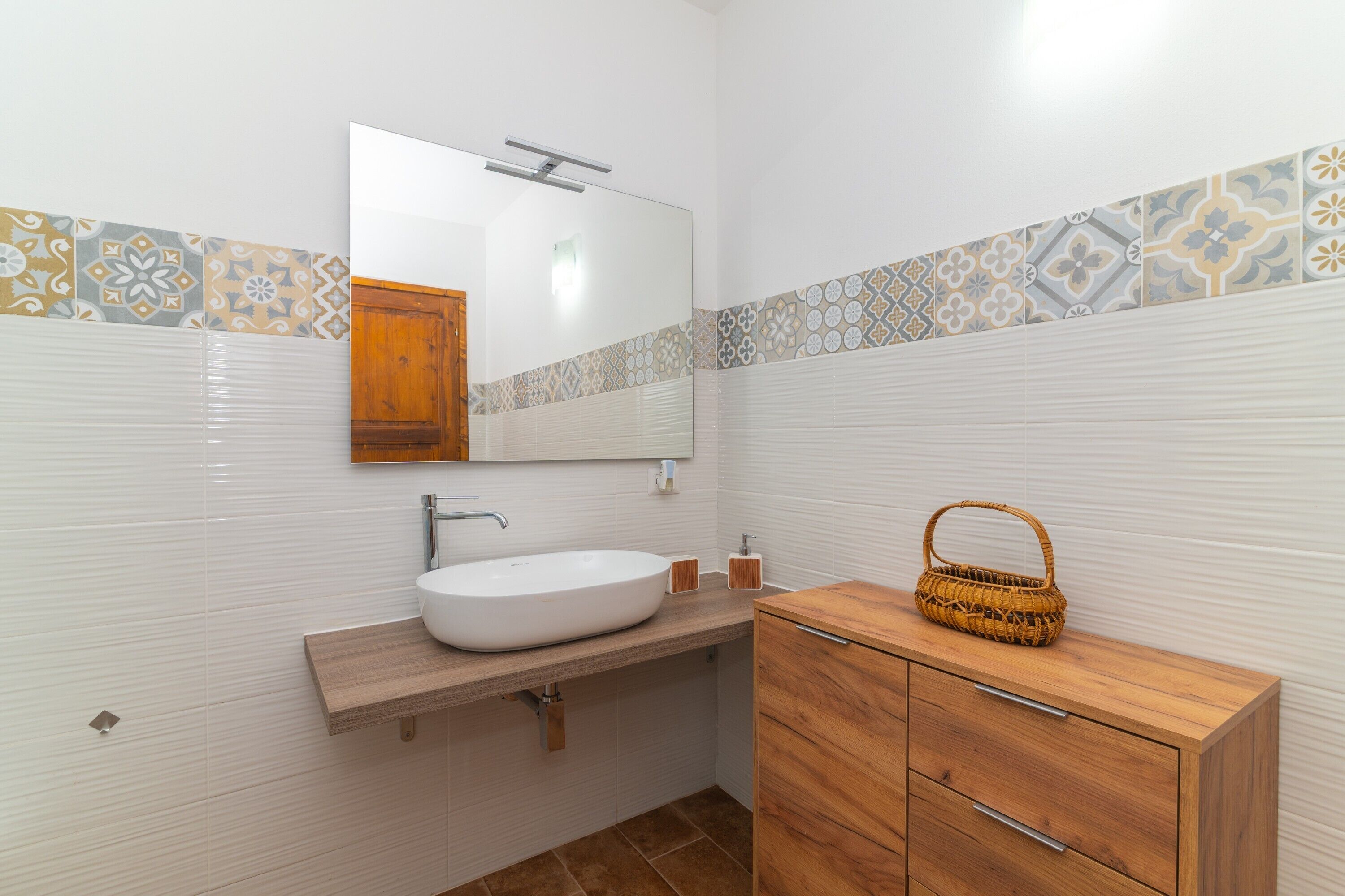A bathroom with a white sink, wooden vanity, and patterned tiles.