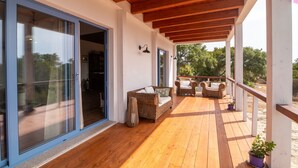 A covered outdoor patio with wooden flooring, a wicker sofa, and a potted plant.
