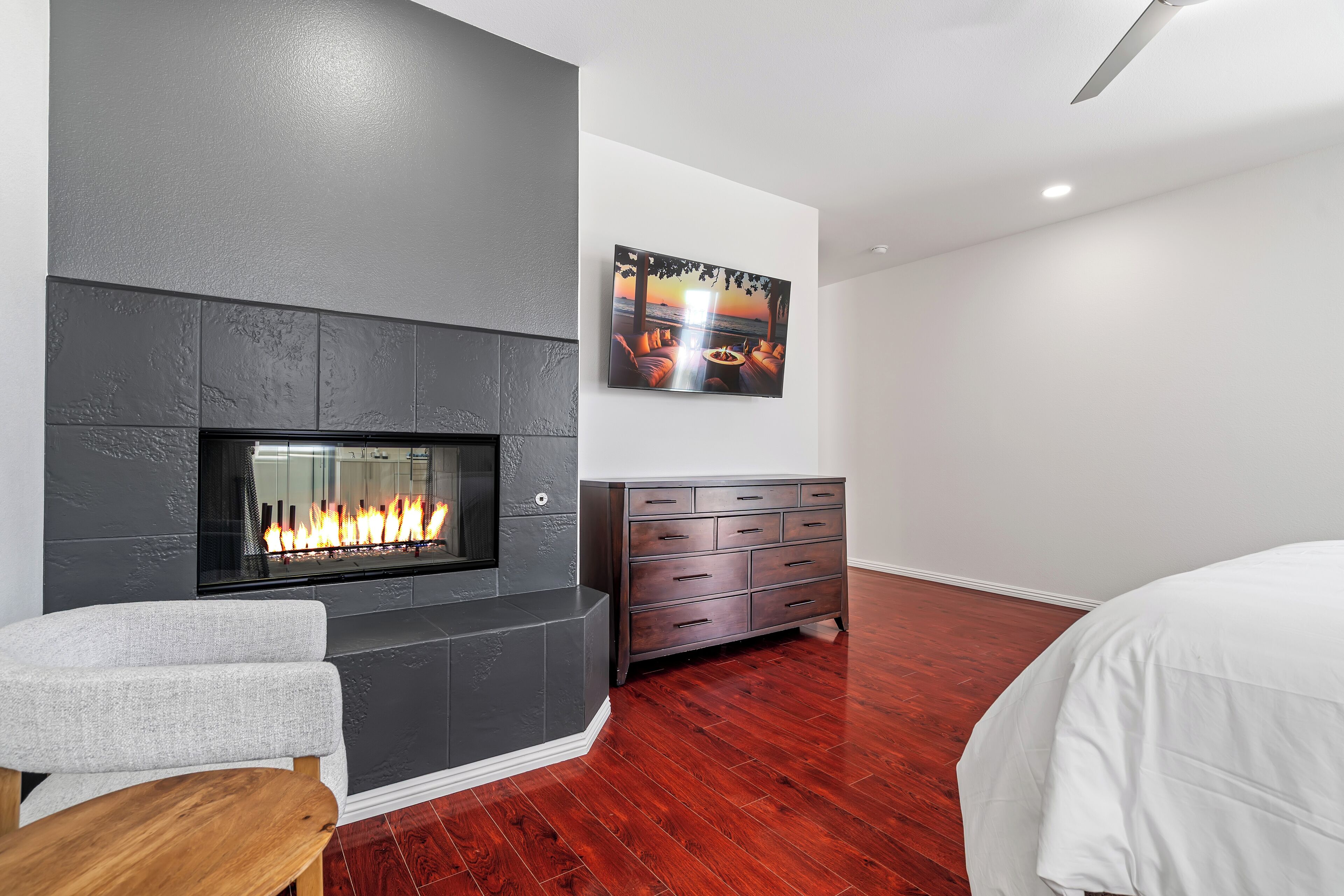 Un dormitorio moderno con chimenea, una cama grande, un aparador y un televisor montado en la pared.