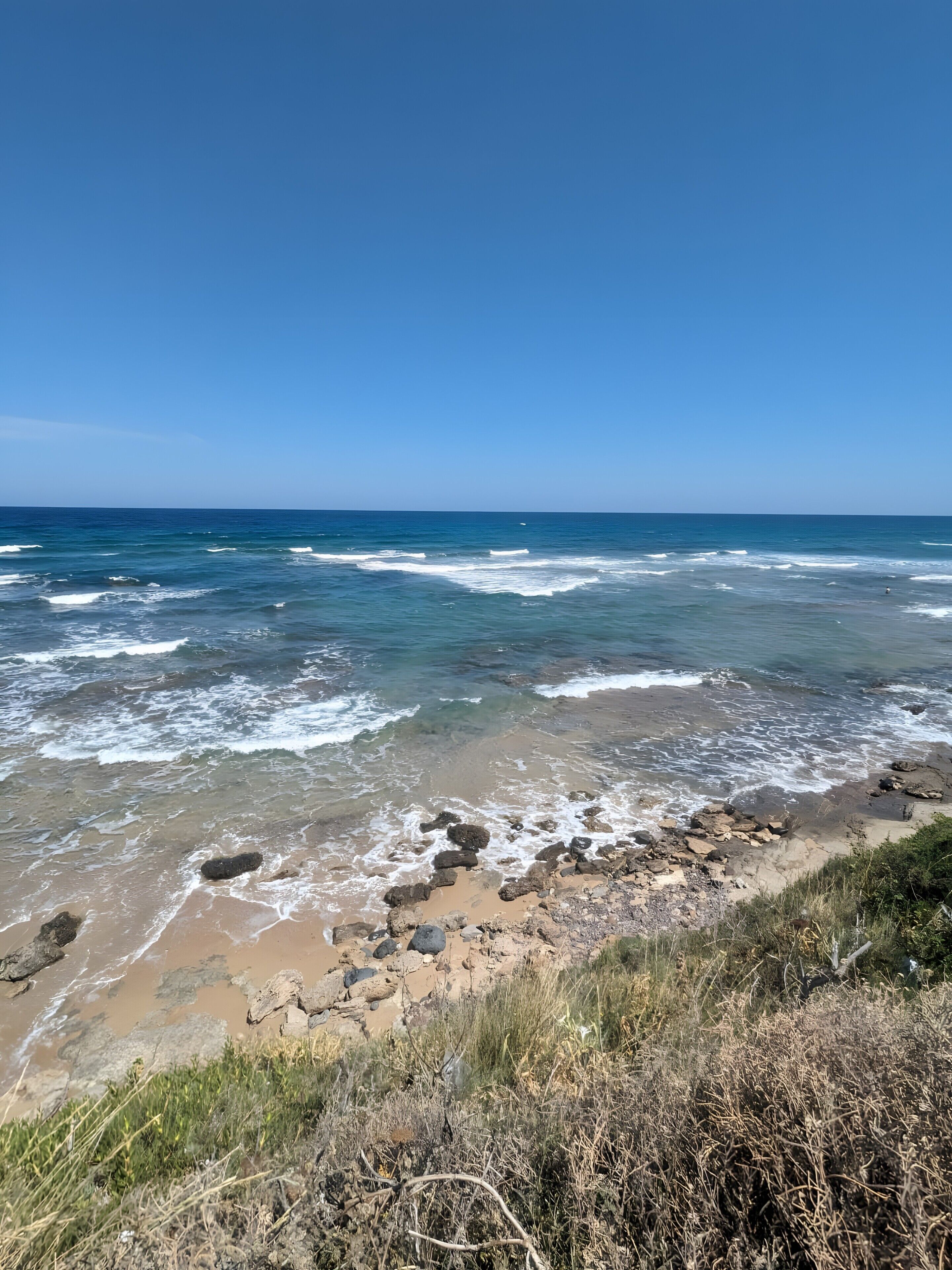 A beach with waves, rocks, and clear sky.