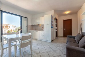 Eine moderne Küche mit weißen Schränken, einem Esstisch mit Stühlen, einer Couch und einem großen Fenster.