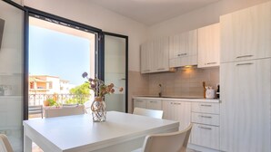 Une cuisine moderne avec des meubles blancs, une table à manger avec des chaises et une vue sur l’extérieur par une porte vitrée.