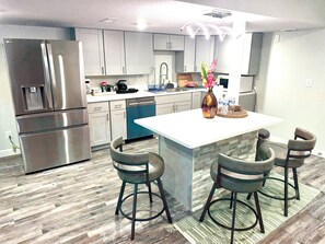 A modern kitchen with stainless steel appliances, a central island with bar stools, and a backsplash with a stone-like texture.
