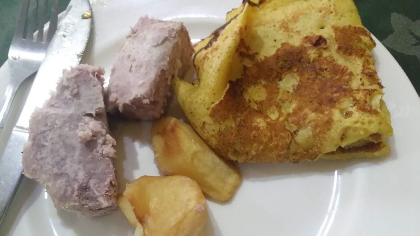 A plate with a folded omelette, a piece of meat, and a few potato wedges.