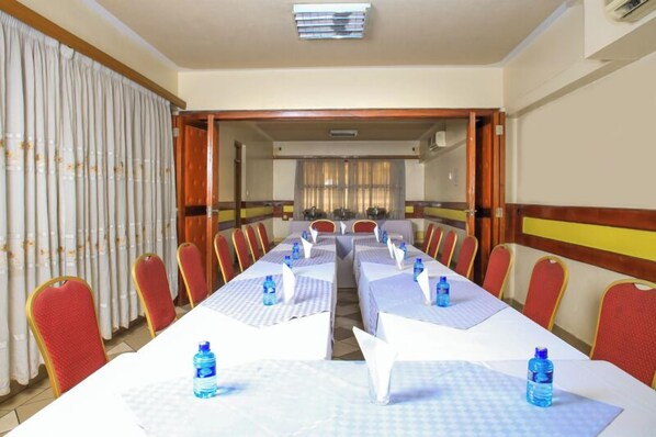 A conference room with long tables, red chairs, and water bottles on the tables.