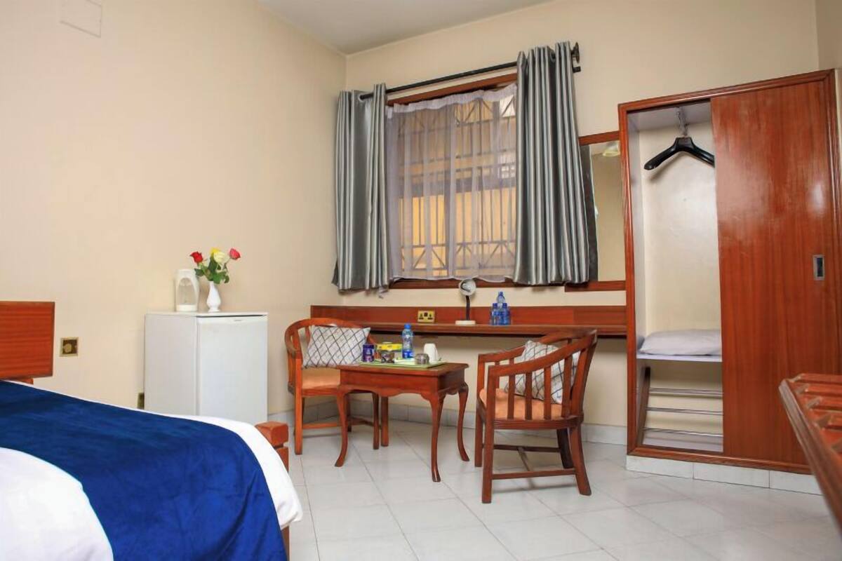 A hotel room with a bed, a desk with chairs, a wardrobe, and a window with curtains.