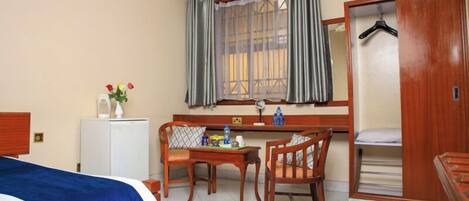 A hotel room with a bed, a desk with chairs, a wardrobe, and a window with curtains.