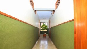 A narrow hallway with green walls and a tiled floor, leading to a room with a window and a potted plant. - Paris Hotel (Nairobi)