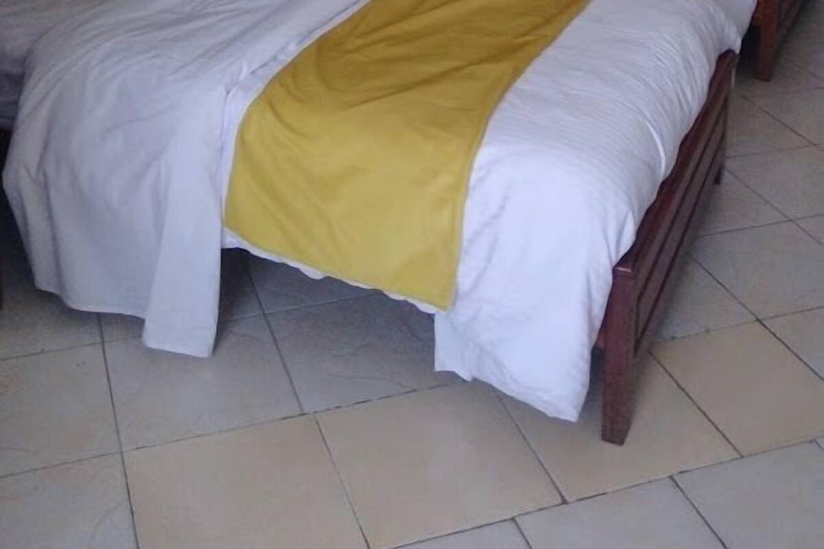 A hotel room with three beds, each with white bedding and yellow pillows. There are white hanging lamps above the beds.