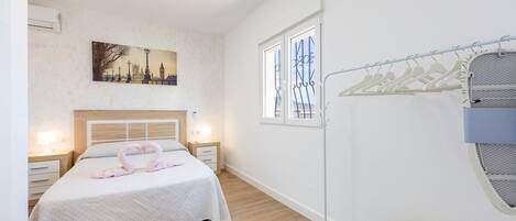 Ein Schlafzimmer mit einem Bett, einem Gemälde, einem Fenster, einem Kleiderständer und einer Wand-Klimaanlage.