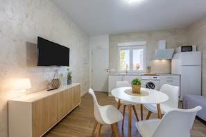 A modern kitchen with a flat-screen TV, a dining area with white chairs, a wooden cabinet, and a washing machine. - Apartment 'La Palmera' with Private Terrace and Air Conditioning (El Nazareno)