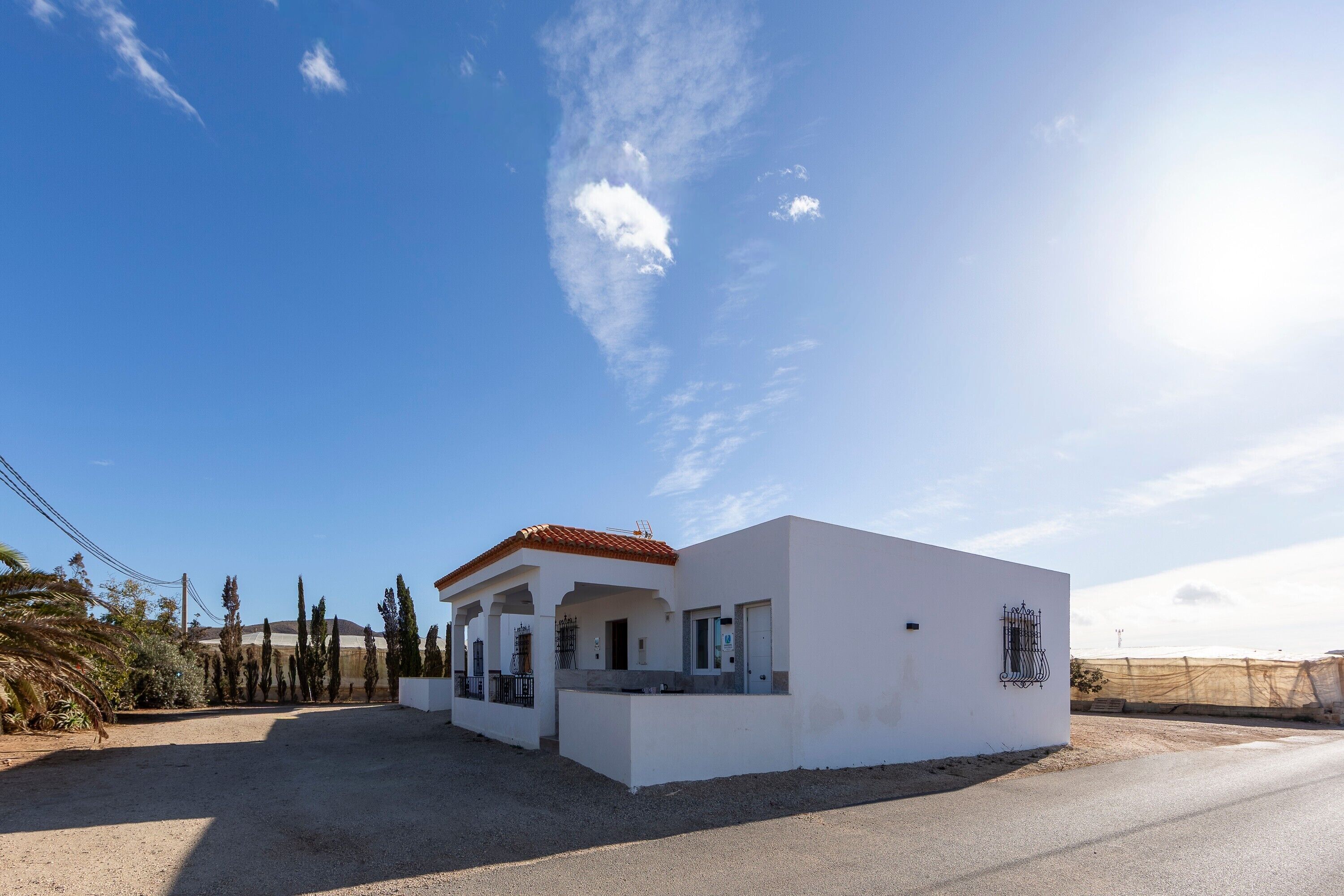 Un bâtiment moderne aux murs blancs, surmonté d’un toit rouge, doté d’un patio couvert et d’une zone délimitée par une clôture.
