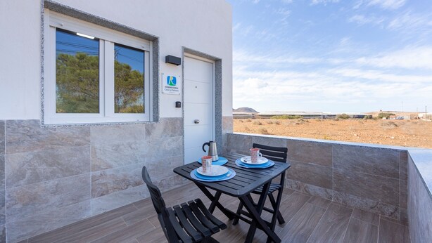 Un balcon avec une table et des chaises, une porte avec une pancarte et une vue sur un paysage désertique.