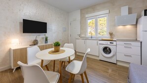 Une cuisine moderne équipée d’un lave-linge, un coin repas avec une table et des chaises, et un téléviseur fixé au mur.