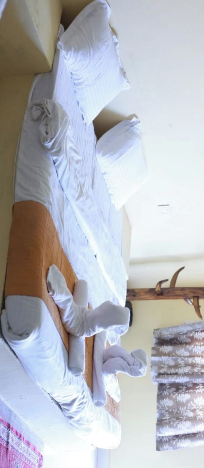 A room with a bed covered in white linens, a wooden headboard, a window with curtains, and a wall-mounted coat rack.