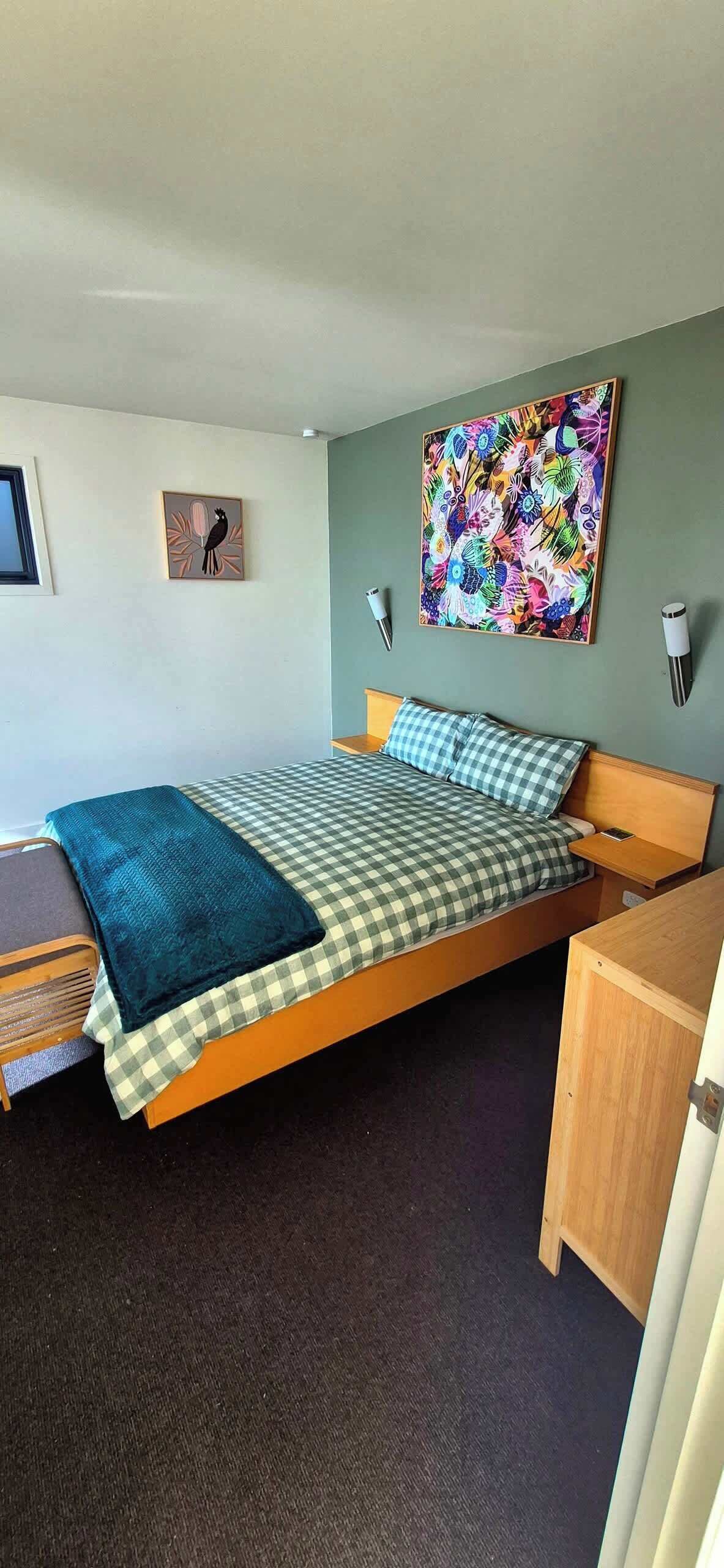A single bed with a checkered bedspread, a teal throw blanket, and a wall-mounted lamp.