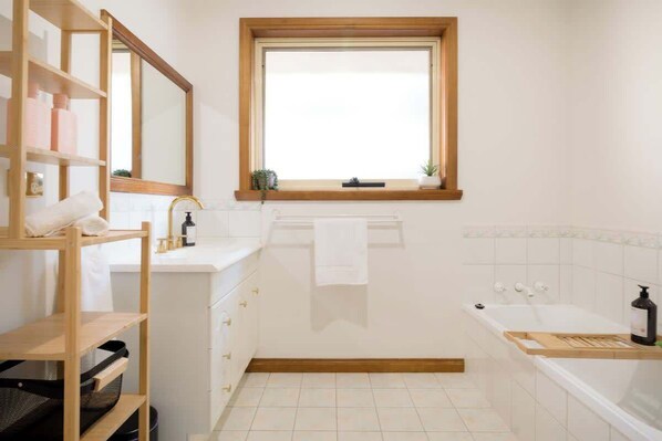 Une salle de bain avec une fenêtre, un lavabo, une baignoire et une étagère contenant des articles de toilette.