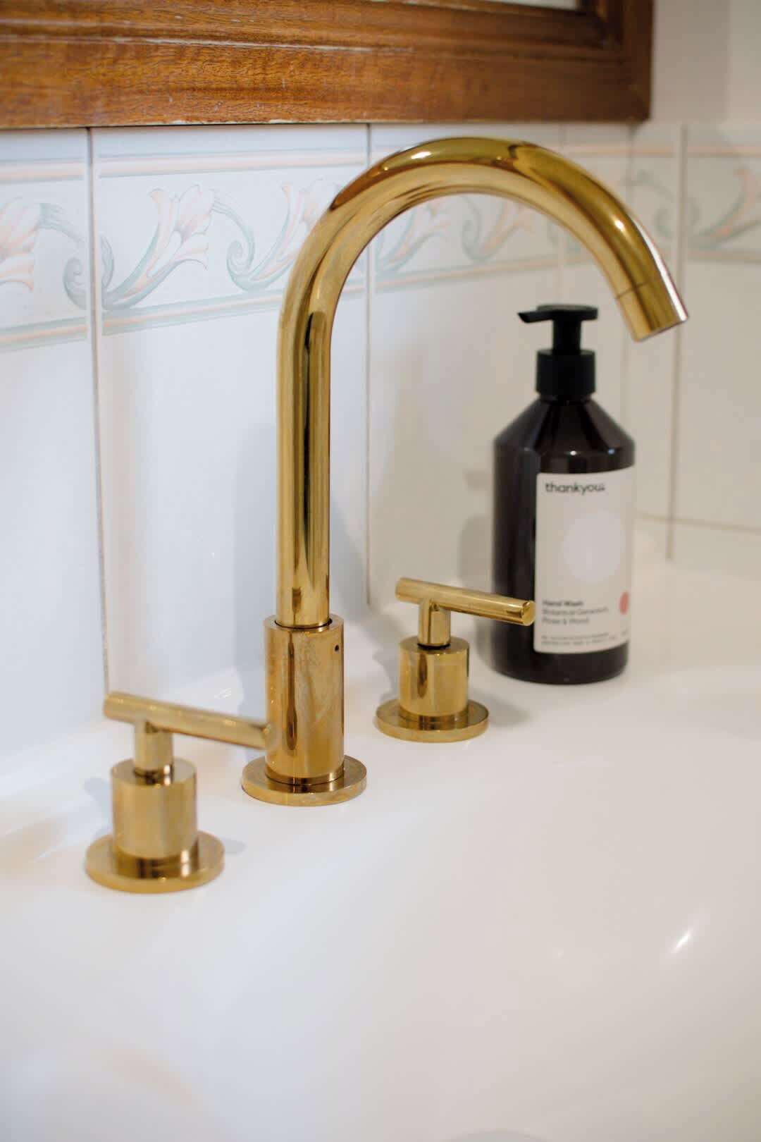 Un baño con grifo dorado, dispensador de jabón y lavamanos blanco.