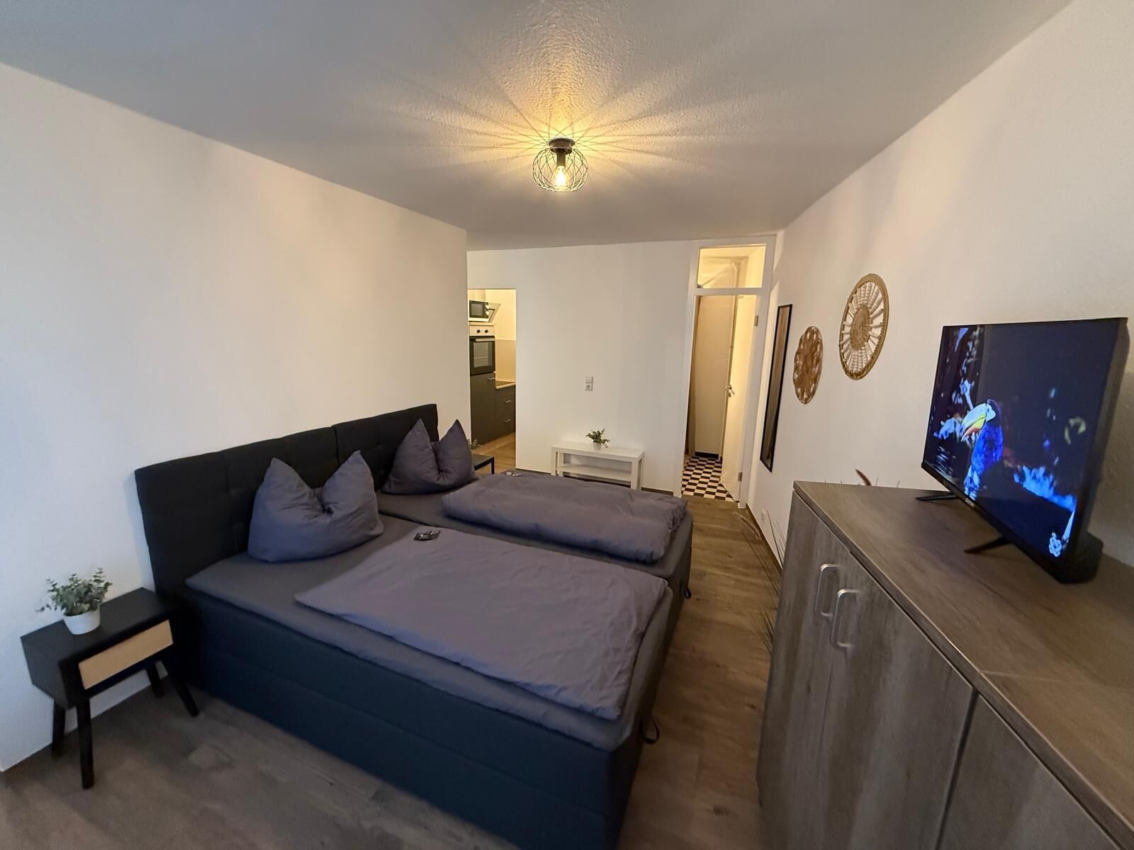 A modern bedroom with two beds, a TV, and a small desk.