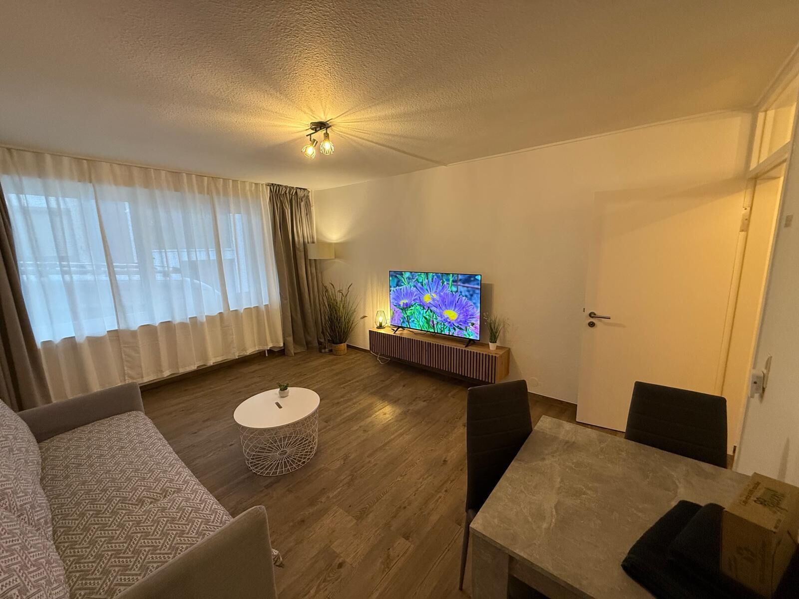 A modern living room with a flat-screen TV, a round coffee table, a sofa, and a dining table.
