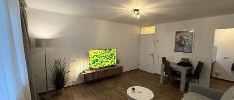 Ein modernes Wohnzimmer mit Fernseher, Essbereich und gemütlicher Sitzecke.