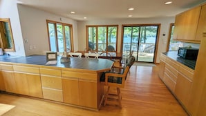 A modern kitchen with a large island, wooden cabinets, and a view to a deck. -  Temple's Sunset Harbor (Newbury)