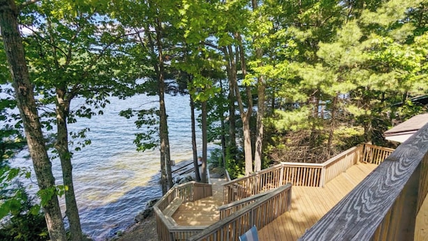 A wooden deck with a railing overlooking a body of water, surrounded by trees. -  Temple's Sunset Harbor (Newbury)