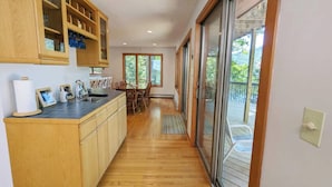 A kitchen with wooden cabinets, a black countertop, and a dining area with chairs and a table. -  Temple's Sunset Harbor (Newbury)