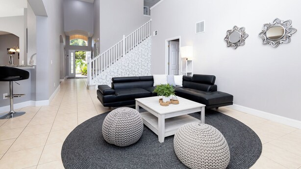 A modern living room with a staircase, black leather sofas, a white coffee table, and two round poufs. - 5BRDisney Villa w/ Pool,Game Room & Resort Access (Kisimmee)