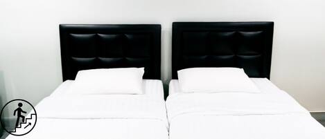 Ein Doppelbett mit schwarzem Kopfteil in einem Zimmer mit weißen Wänden. An der Wand hängen zwei Bilder, eines grün und eines orange.