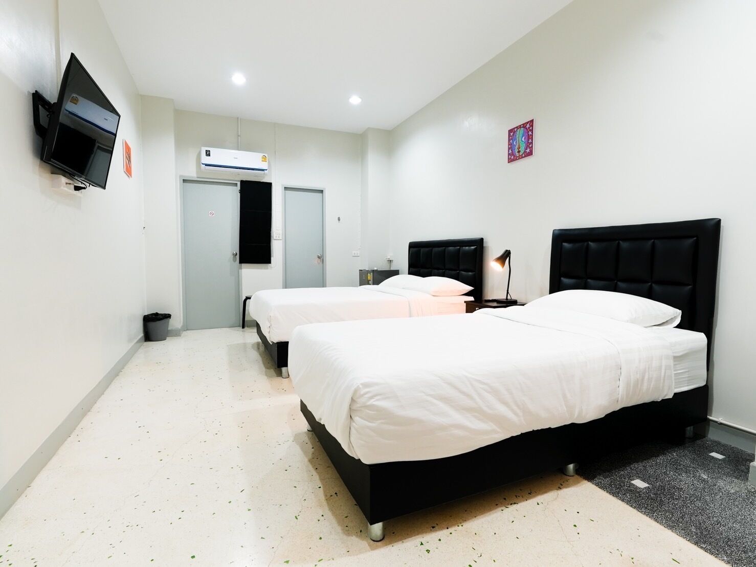 Une chambre d’hôtel avec deux lits, une télévision, un appareil de climatisation et une porte.