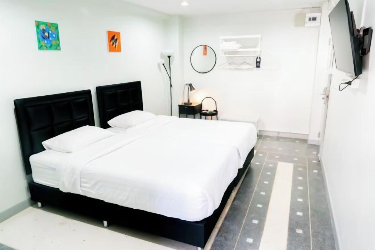 A hotel room with a large bed, a desk with a chair, a flat-screen TV mounted on the wall, and artwork on the walls.