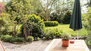 Eine Garten-Terrasse mit einem Holztisch, einem grünen Sonnenschirm und einem Blumentopf.