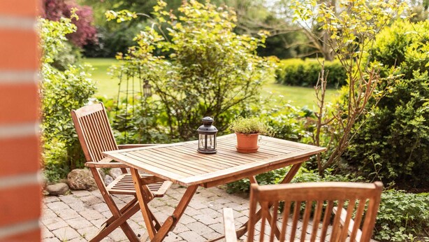 Een houten tafel met stoelen buiten, met een lantaarn en een potplant erop.