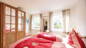 A bedroom with two beds, a wooden wardrobe, and a large window with curtains.
