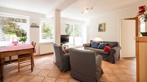 A spacious living room with a large window, a television, a sofa, and a dining area with a table and chairs.
