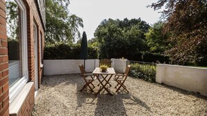 A patio with a table and chairs, surrounded by a gravel ground and a white wall.