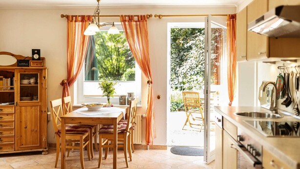 A cozy kitchen with wooden cabinets, a dining area with a table and chairs, and a view of a garden through a glass door.