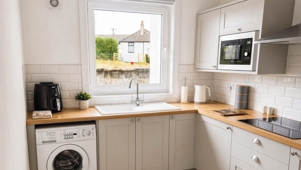 Une cuisine compacte équipée d’un lave-linge, d’un four à micro-ondes et d’une fenêtre donnant sur une maison.