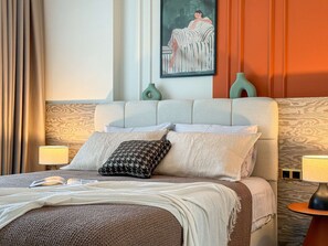 Une chambre d’hôtel bien aménagée, avec un grand lit, deux tables de chevet avec des lampes, un tableau au mur et un tapis à motifs.